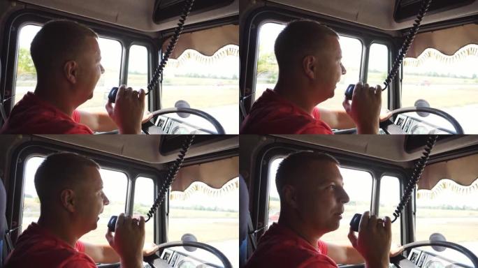卡车司机在晴天开车时通过无线电通讯讲话。卡车司机骑在乡间小路上，用对讲机说话。物流和运输的概念。关闭
