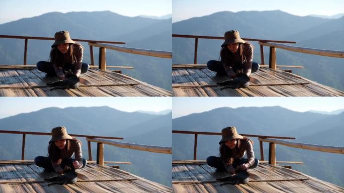 一个女旅行者在蓝天美丽的山景木制阳台上坐着和猫玩耍的慢动作