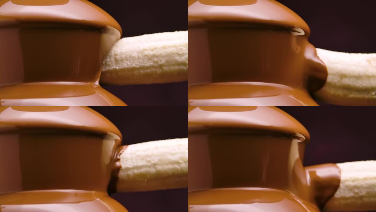 融化的牛奶巧克力在巧克力喷泉中流动。将成熟的香蕉浸入并包裹在从叶栅流下来的热液体巧克力中。火锅。派对