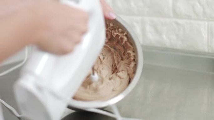 女性专业糖果手拿着手动搅拌器，浸入巧克力黄油奶油中。打奶油给甘纳奇。烘焙工艺阶段