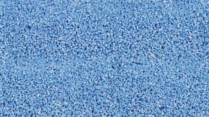 由聚丙烯制成的次级颗粒，蓝色塑料颗粒碎到桌子上。工业用颗粒塑料原料。聚合物树脂。生塑料回收概念。