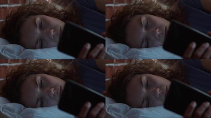 哭泣的女人躺在枕头上，用于电话。手里拿着电话的女人流泪了。人的心理状态