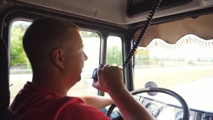 卡车司机在晴天开车时通过无线电通讯讲话。卡车司机骑在乡间小路上，用对讲机说话。物流和运输的概念。关闭