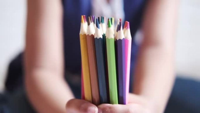 儿童手握许多彩色铅笔
