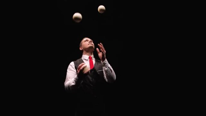 一个专业杂耍白球的时尚男人的轨道镜头。被灯光照亮的马戏团表演者在黑色工作室背景上投掷并接球。特写。慢
