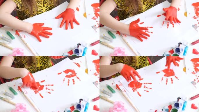 小女孩玩得开心，画她的手。有趣的孩子用红色油漆画脏手。