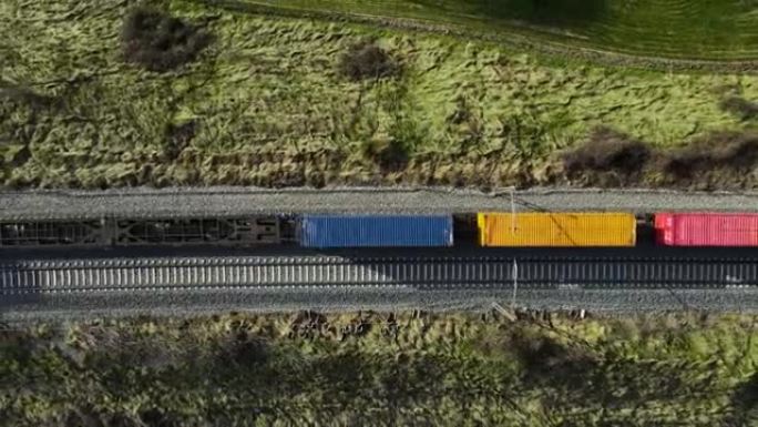货运列车的空中俯视图，载有五颜六色的集装箱，在日落时穿过森林。无人机拍摄的4k镜头。高质量4k镜头