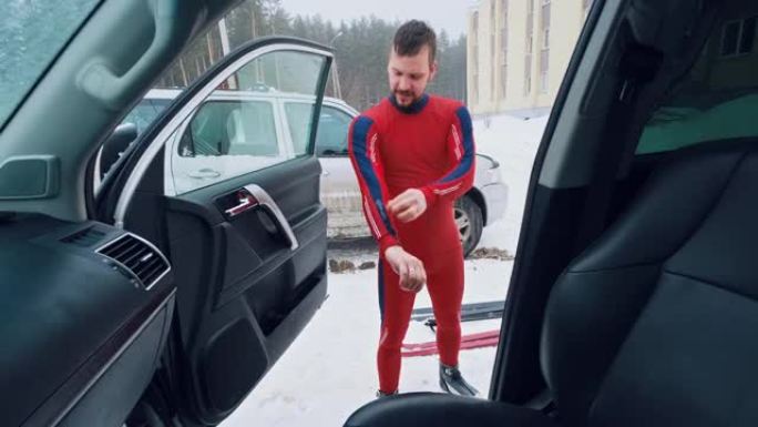 滑雪者穿上西装。年轻人站在停车场上，给自己穿上滑雪服。从汽车上看