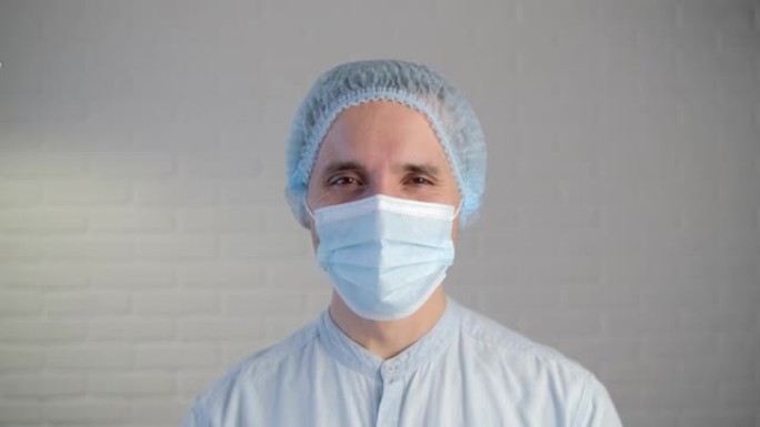 大流行期间戴着防护口罩的男医生。疲惫的医生透过面具微笑着向前看。