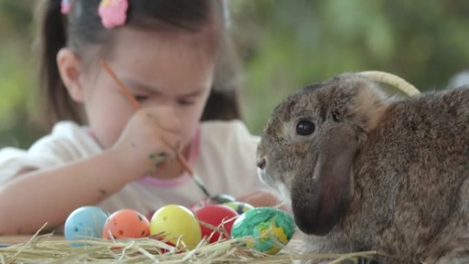亚洲女孩为复活节彩蛋着色时，复活节节日餐桌上的兔子