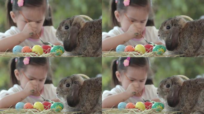 亚洲女孩为复活节彩蛋着色时，复活节节日餐桌上的兔子