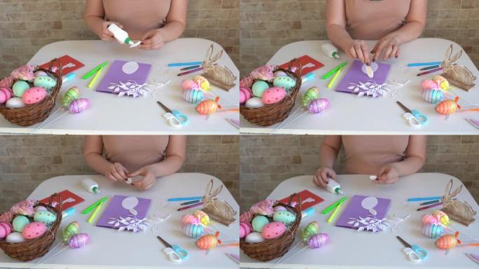 女人为复活节做工艺品。彩色纸制作的彩色手工卡片。剪刀，纸板，鸡蛋，兔子。木桌上的艺术创意