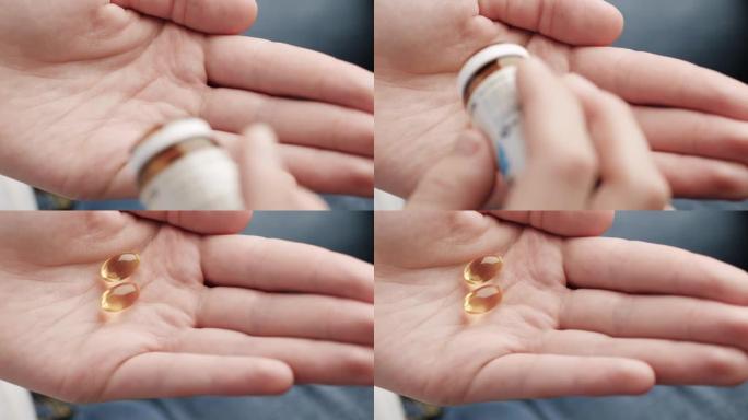 两个透明的大琥珀色椭圆形药丸胶囊从药瓶落入手掌。特写，顶视图
