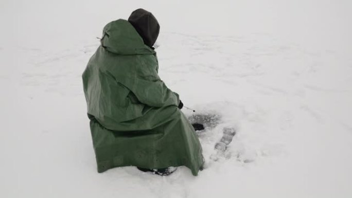 冬季钓鱼。人正在冰洞里抓鱼。带鱼竿的渔夫在冰冻的湖上用鱼竿抓鱼