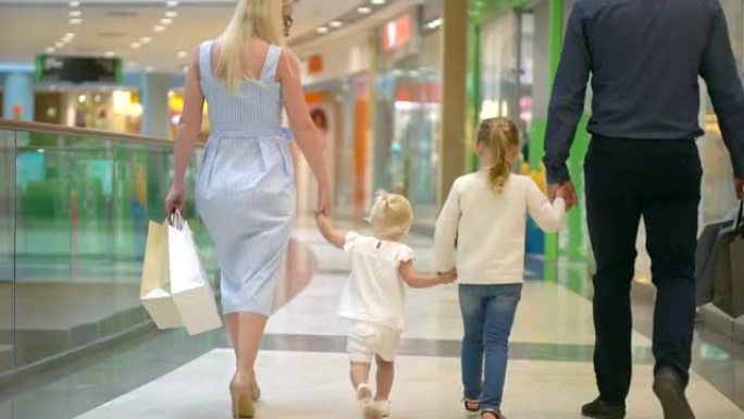 幸福的四口之家购物。商场里的家庭。和父母在购物中心的孩子。家庭在大商店购物。一家人背着购物袋穿过购物