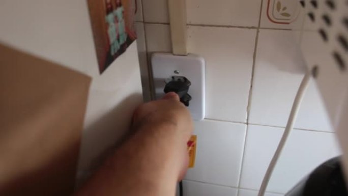 一只手在厨房墙壁的电源插座中连接电源线