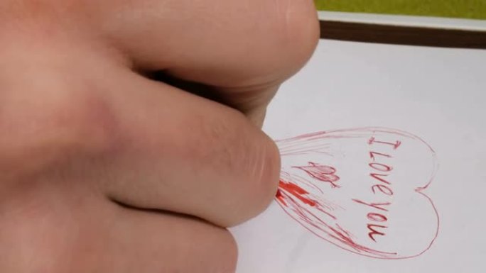 一个年轻人为他的女朋友画了一张情人卡。一个年轻人的手的特写镜头他用红笔在纸上写下我爱你的话