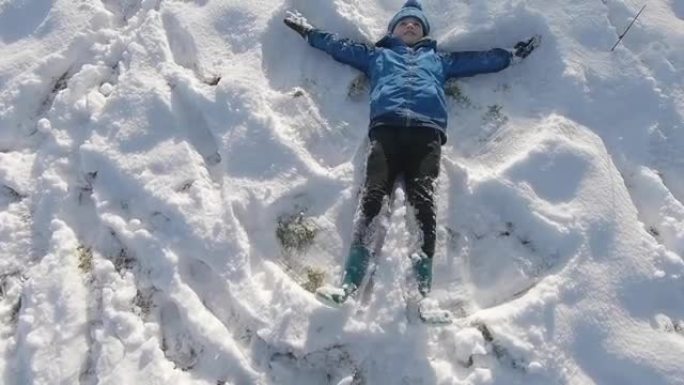 一个小男孩在新鲜的雪中向后倒下，用胳膊和腿做一个雪天使