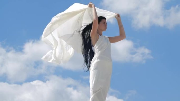 一个美丽的黑发女人，长发，穿着白色飘动的衣服站在山顶上，靠着天空。天使存在的海市蜃楼。200 fps