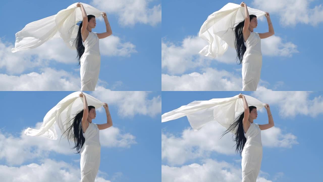 一个美丽的黑发女人，长发，穿着白色飘动的衣服站在山顶上，靠着天空。天使存在的海市蜃楼。200 fps