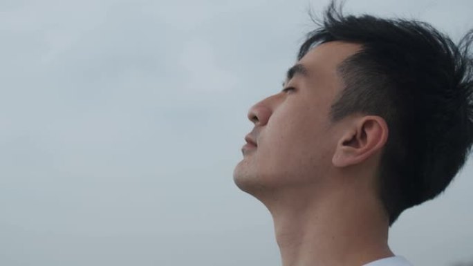 英俊的亚洲男子旅行者闭上眼睛，在海景呼吸新鲜空气。健康健康生活方式概念。