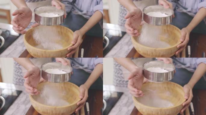亚洲夫妇的亲密手互相帮助，在家里的厨房里，在浪漫的氛围中制作面包店。年轻人一起工作，将配料混合在木碗