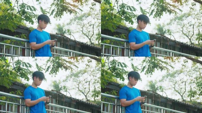 运动男子在跑步后站在公园的围栏上，使用智能手机检查社交媒体并在智能手机上发短信给朋友。