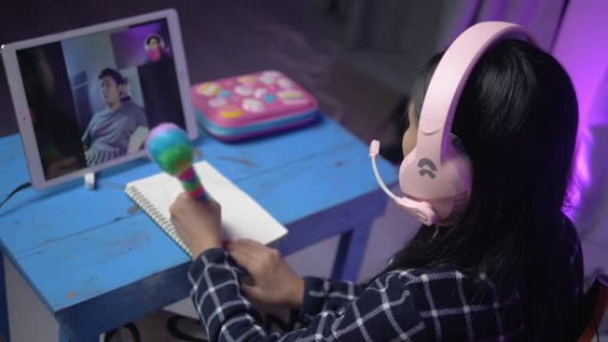 亚洲女学生在家通过数字平板电脑与老师进行视频通话，背景为发光二极管，社交疏远生活理念。