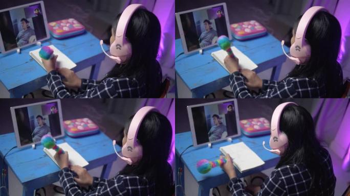 亚洲女学生在家通过数字平板电脑与老师进行视频通话，背景为发光二极管，社交疏远生活理念。