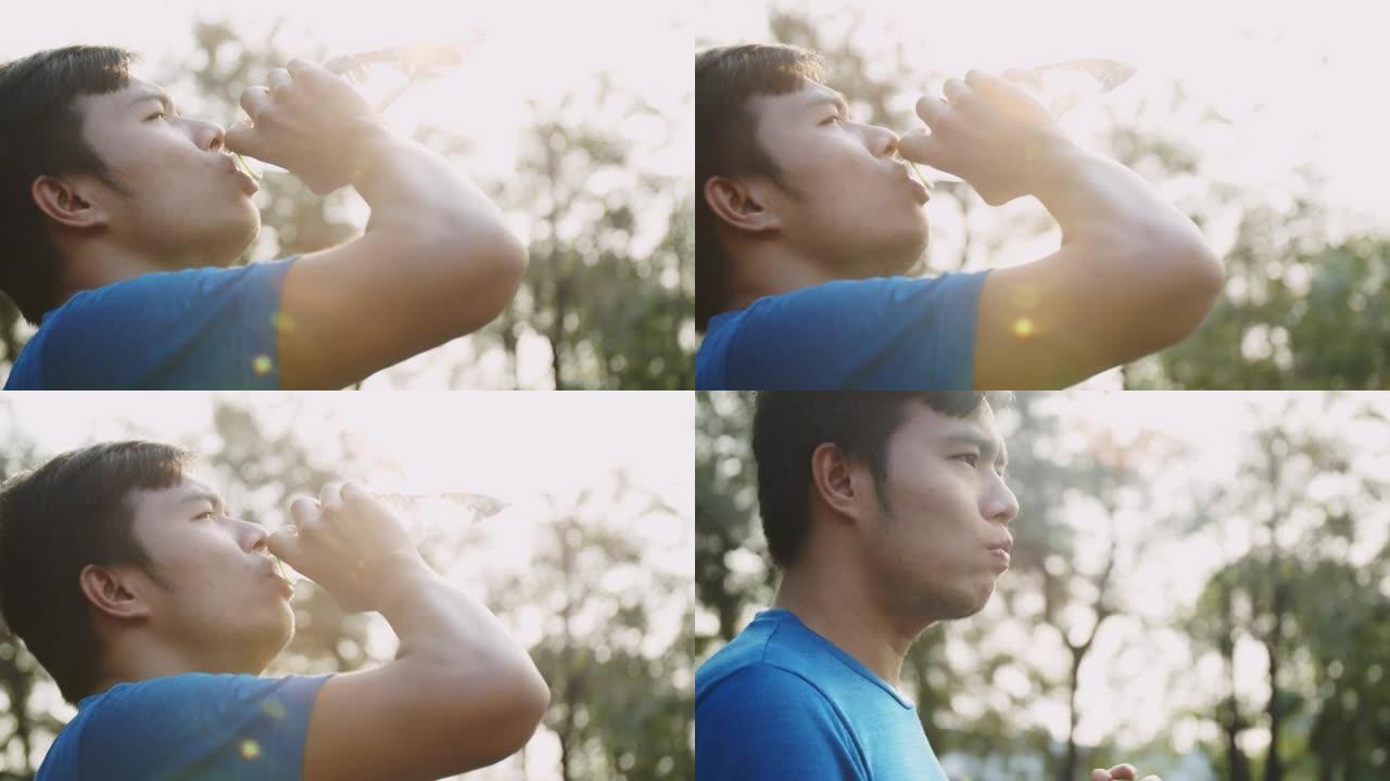 亚洲男子运动员跑步者休息一下，在下午晚些时候用镜头闪光喝水。