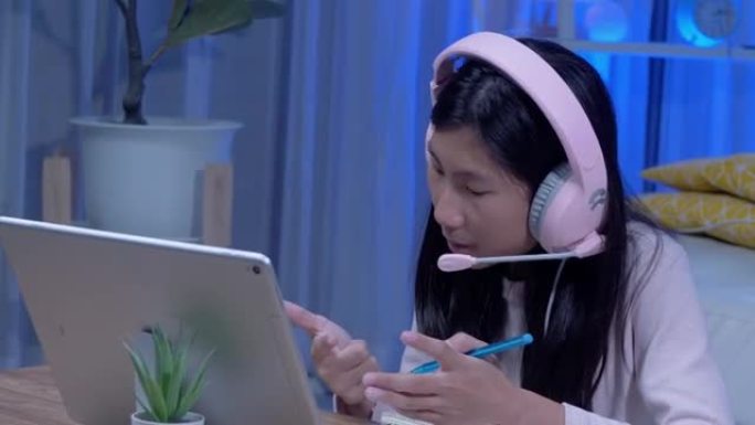 快乐的亚洲女孩使用耳机和麦克风通过数字平板电脑与老师和朋友交流，在新型冠状病毒肺炎期间进行家庭教育，