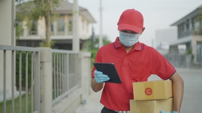 穿着红色制服的男性送货员正在寻找当前正在运送的房屋，从您持有的平板电脑中搜索门牌号。新的正常概念。