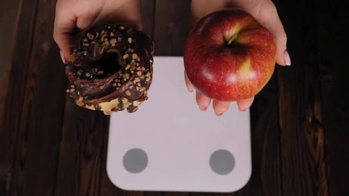 一个女人站在秤上时拿着苹果和甜甜圈的特写镜头。