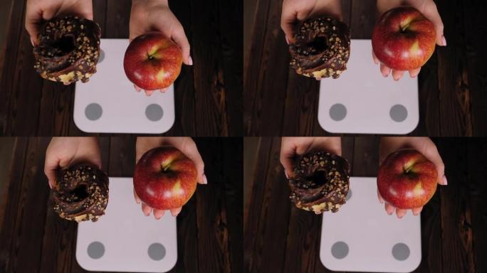 一个女人站在秤上时拿着苹果和甜甜圈的特写镜头。