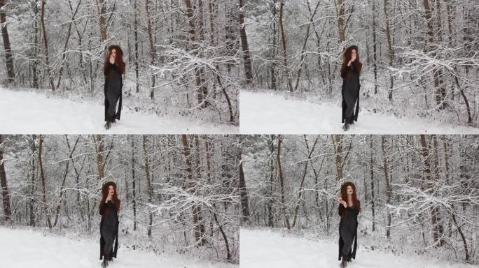 一个穿着黑色连衣裙的红色长发的年轻女孩在寒冷的白雪皑皑的森林中呼吸温暖双手