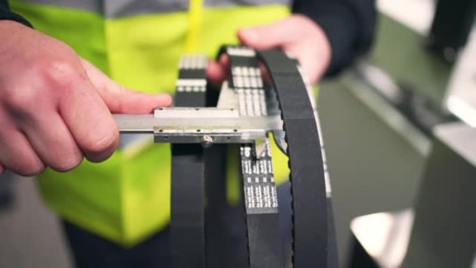 年轻的男性工厂工人用卡尺测量橡胶带的宽度