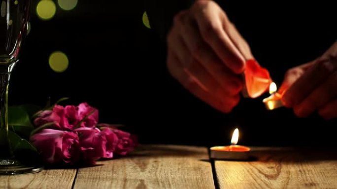 男人的手燃烧蜡烛的特写镜头，并将它们放在两个酒杯和玫瑰旁边的桌子上