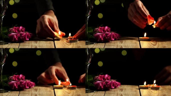 男人的手燃烧蜡烛的特写镜头，并将它们放在两个酒杯和玫瑰旁边的桌子上