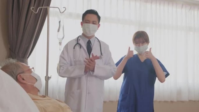 亚洲医生和护士通过微笑拍手鼓励躺在床上的生病老人。在医院大流行期间，患者和医生团队戴着口罩防止新型冠