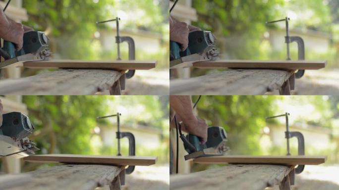 老人木匠用电动刨床在木器上工作，在车间生产家具。在家工作。