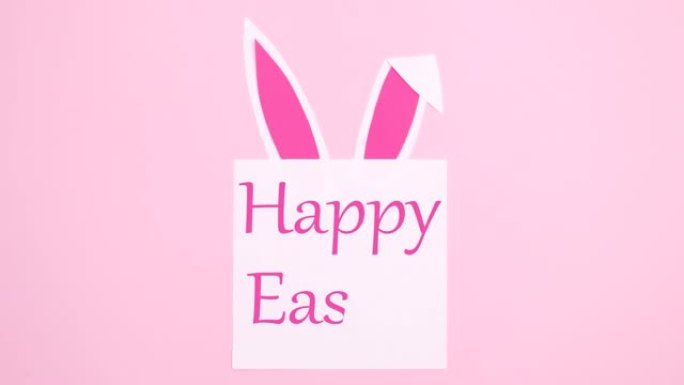 复活节快乐的文字写在纸上，兔子耳朵在柔和的粉红色背景上。停止运动