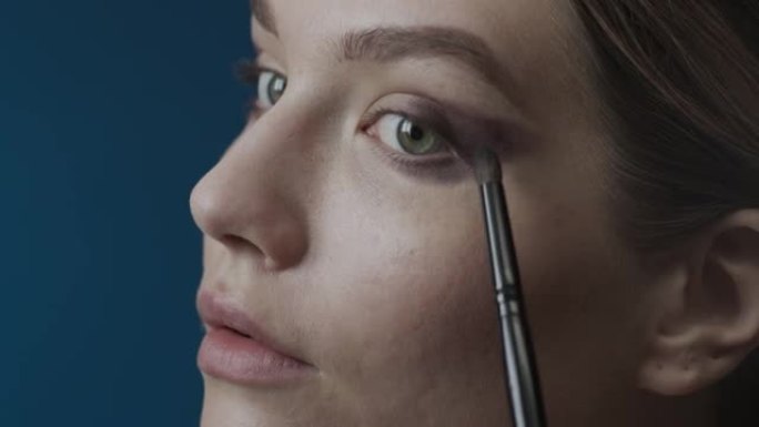 化妆申请的步骤。一个女孩的脸用化妆刷在眼睑上涂抹烟熏眼影的特写镜头。