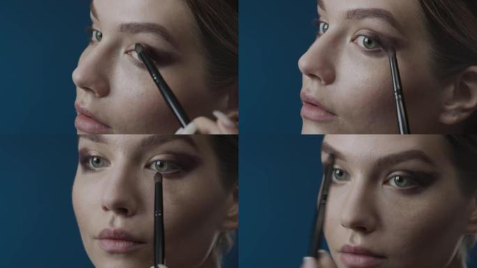 化妆申请的步骤。一个女孩的脸用化妆刷在眼睑上涂抹烟熏眼影的特写镜头。