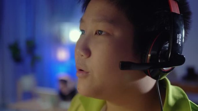 快乐的亚洲男孩使用耳机和PC电脑在夜间与朋友在家玩网络游戏，带led灯，生活方式理念。
