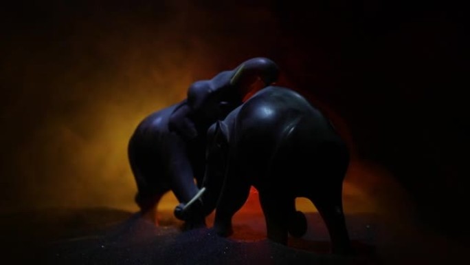 火焰背景上的大象战斗剪影或两只大象公牛在战斗时互动和交流。创意餐桌装饰，彩色背光带雾。选择性聚焦