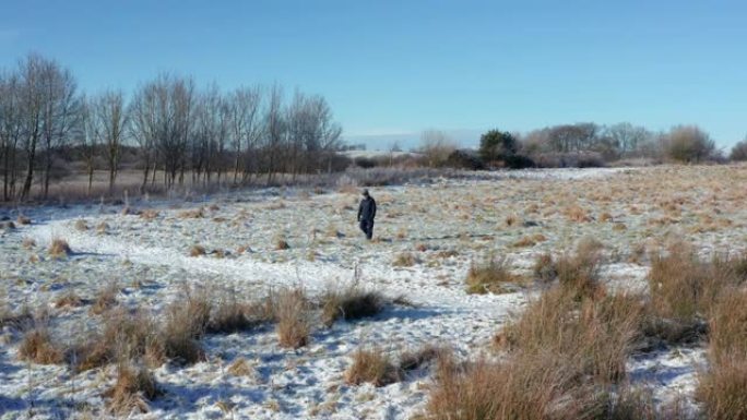一名高级男子独自走向苏格兰西南部积雪覆盖的人行道的无人机的景色