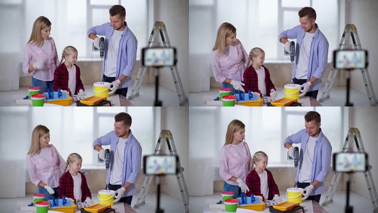 家庭博客，可爱的开朗的父母和可爱的女儿将染料倒入油漆桶中，并录制有关在房间完成工作期间在智能手机相机