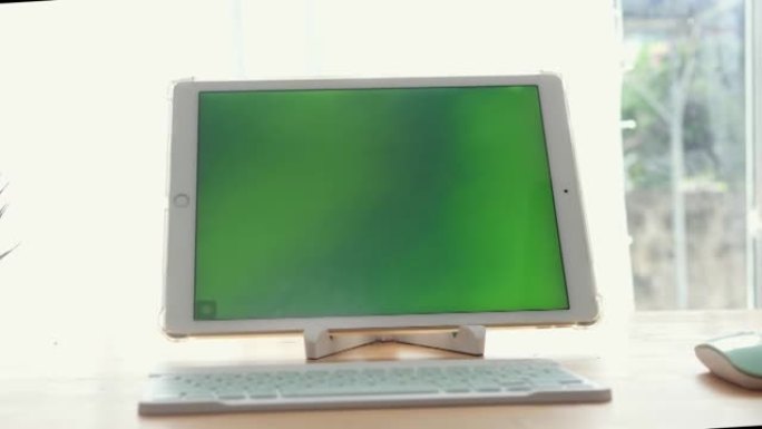 绿色屏幕数字平板电脑，键盘和电脑鼠标放在家里靠近窗户的桌子上，技术概念。