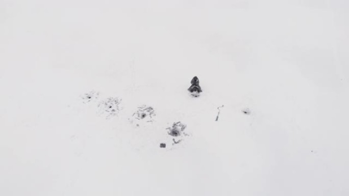 渔夫正在冰冻的河上的冰洞里抓鱼。男子在冬季钓鱼时独自钓鱼，空中无人机射击。