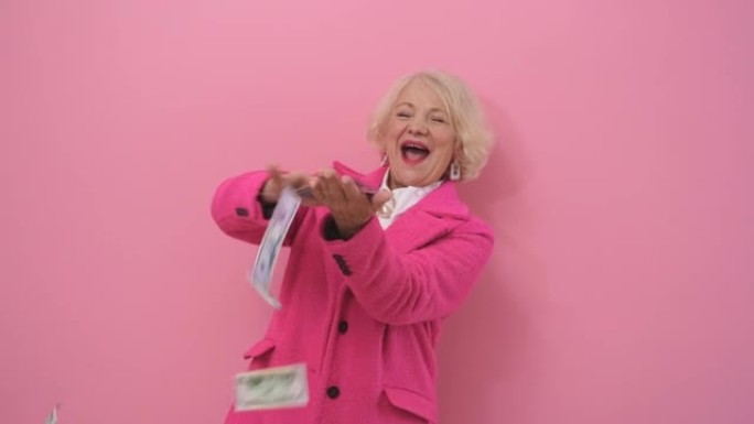 一个穿着时髦的粉红色外套的有钱，优雅的女人扔掉了钱，把钱花在了粉红色背景隔离的无用物品上